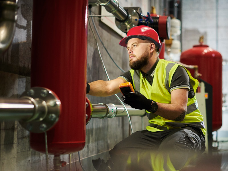 A technician in a red hard hat and safety yellow vest inspecting a fire safety system