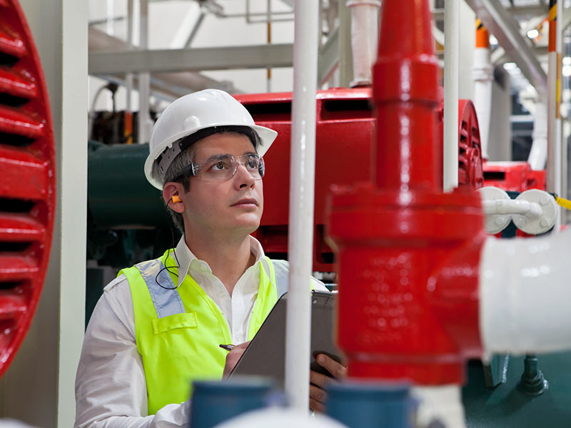 A man in a hardhat and safety glasses inspecting a fire safety system.