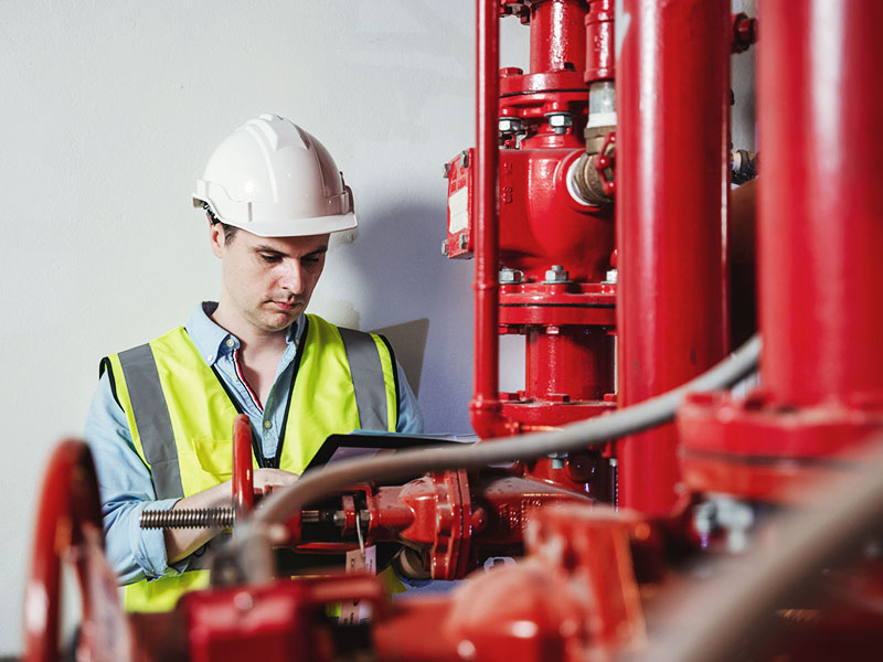 Man in hard hat and vest inspecting red fire pump pipes