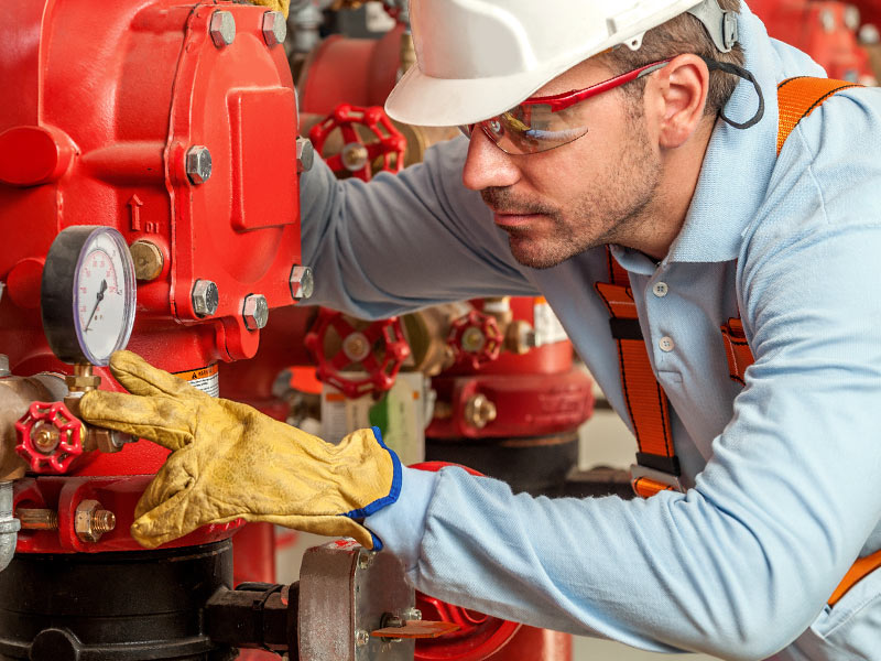 A man in safety glasses and a hardhat inspects the gauge on a fire sprinkler system
