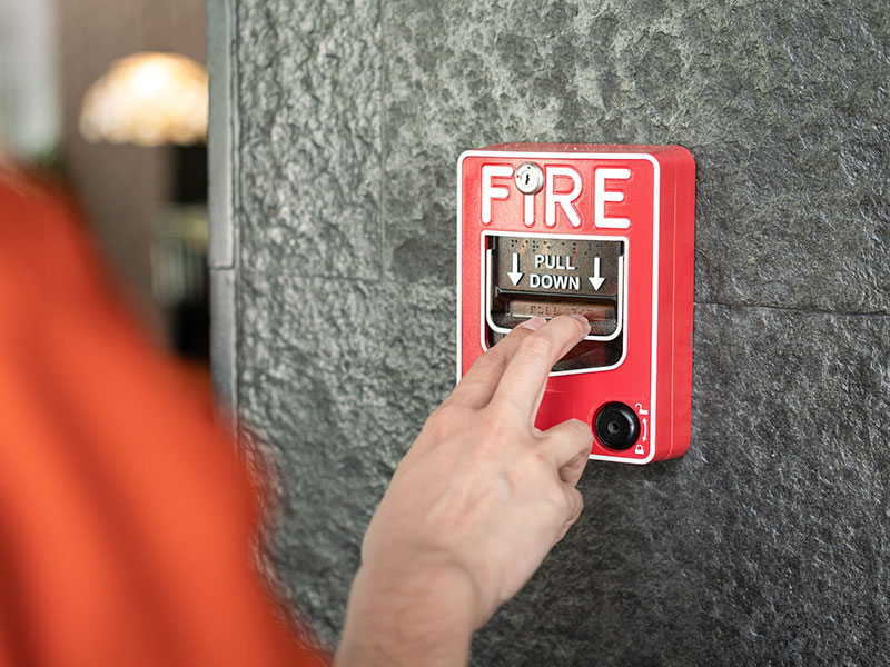 The hand of a life safety professional pulls down the lever on a fire alarm for testing purposes